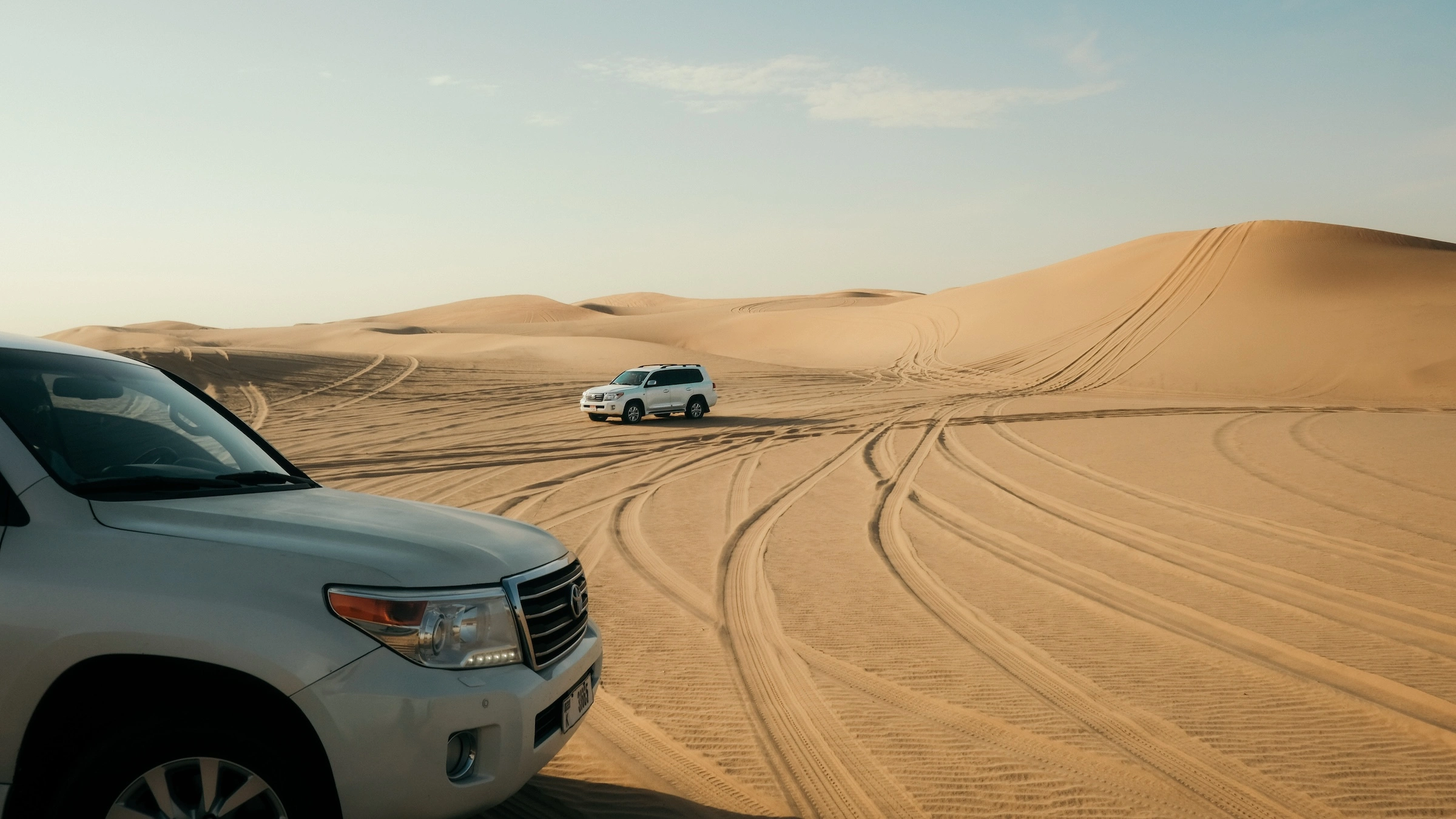 an image of two land cruiser 4x4 parked in the desert with a large sand dune nearby